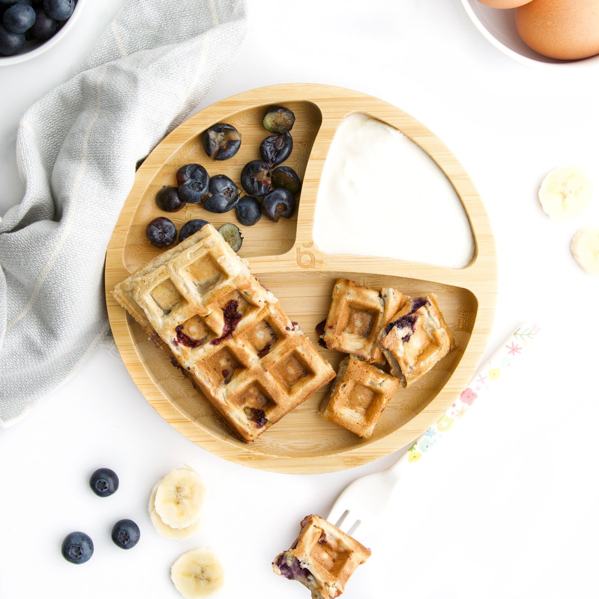 Baby Friendly Banana and Blueberry Waffles on Baby Plate Served With Yogurt and Smashed Blueberries. 