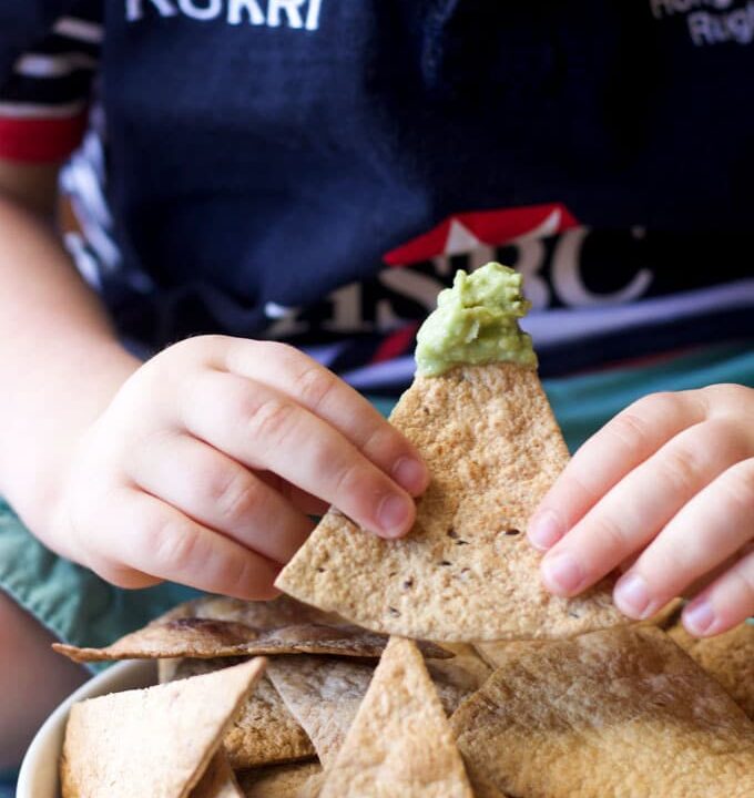 Child Holding Baked Tortilla Chip Dipped in Guacamole