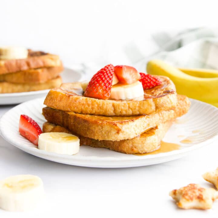 3 Slices of Banana French Toast Stacked on Plate Topped with Banana and Strawberry.