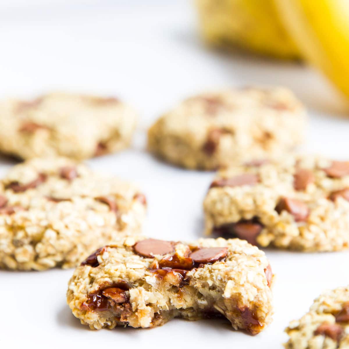 Close Up Side Shot of Banana Oatmeal Cookie with Bite Removed. Banana Oat Cookies and Bananas in Background. 