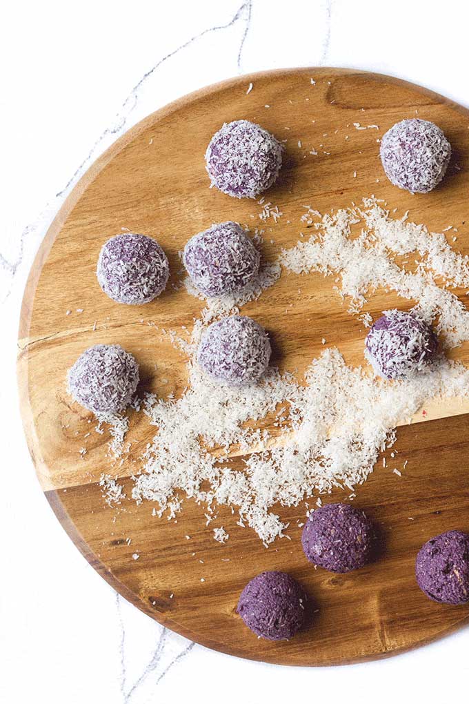 Top Down Shot of Blueberry Breakfast Balls on Wooden Board. Some Coated in Coconut, Others Left Uncoated.