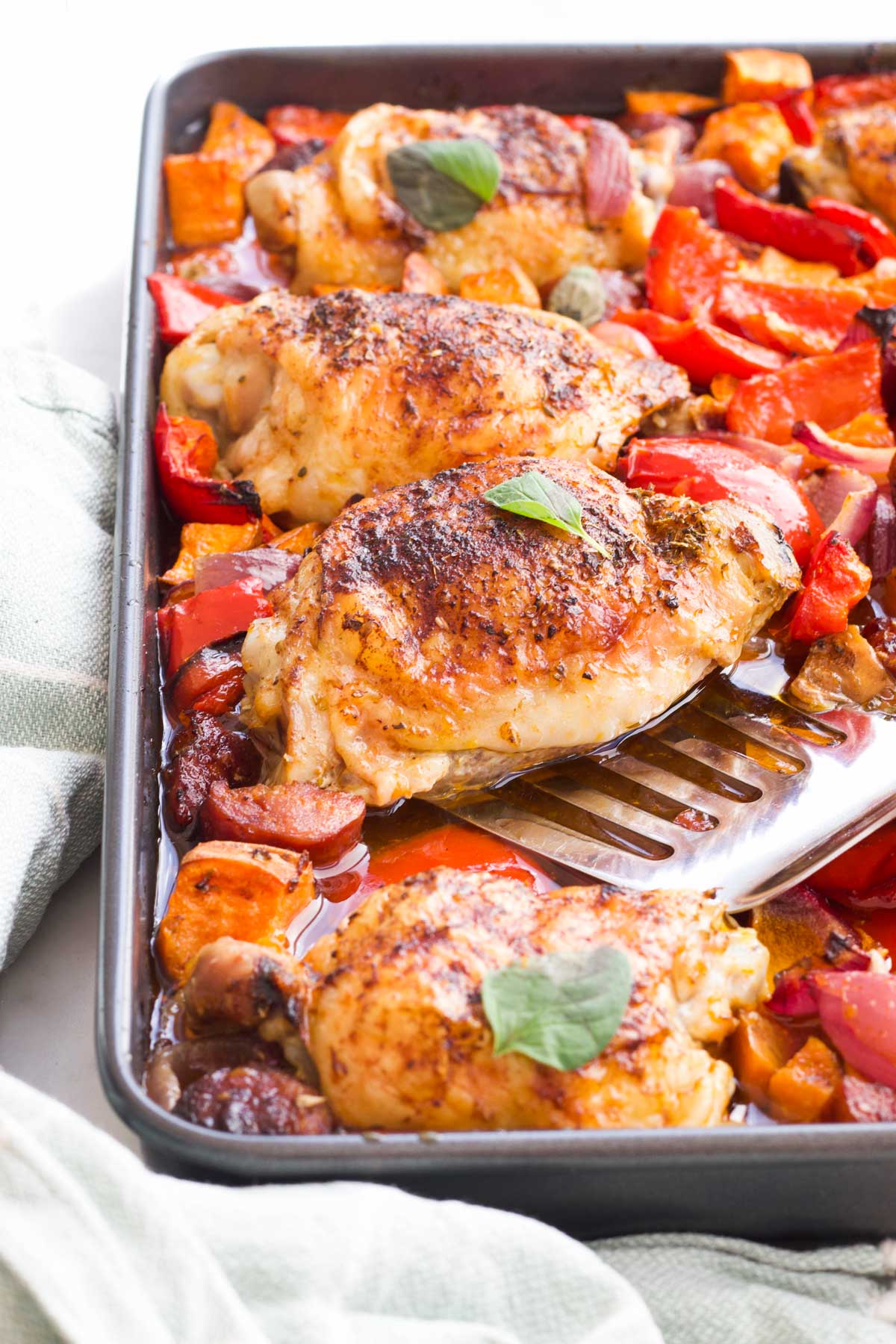 45 Degree Angle Shot of Chicken Chorizo Tray Bake with Fish Slice Removing Chicken Thigh from Tray.