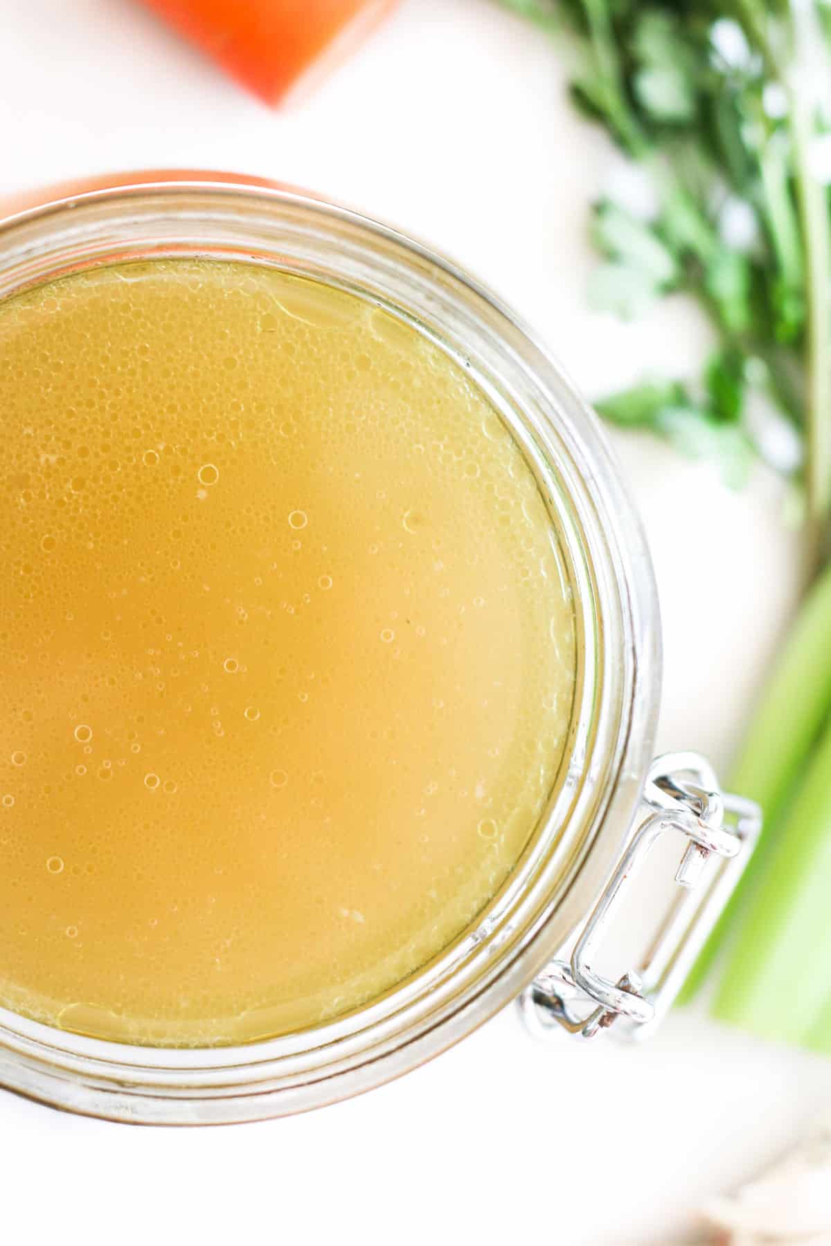 Top Down Shot of Chicken Stock in Glass Jar with Chicken and Vegetables Scattered Around the Background.