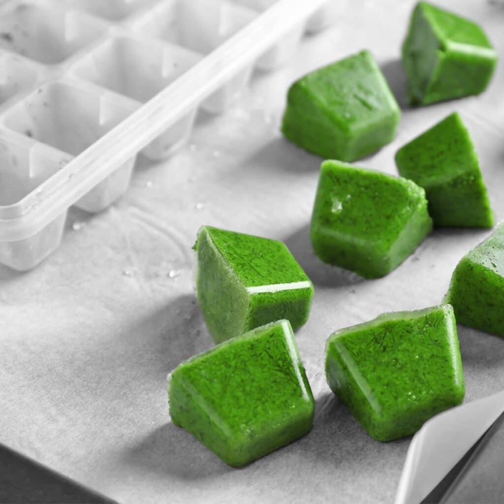 Frozen Cubes of Green Baby Puree Next to IceCube Tray