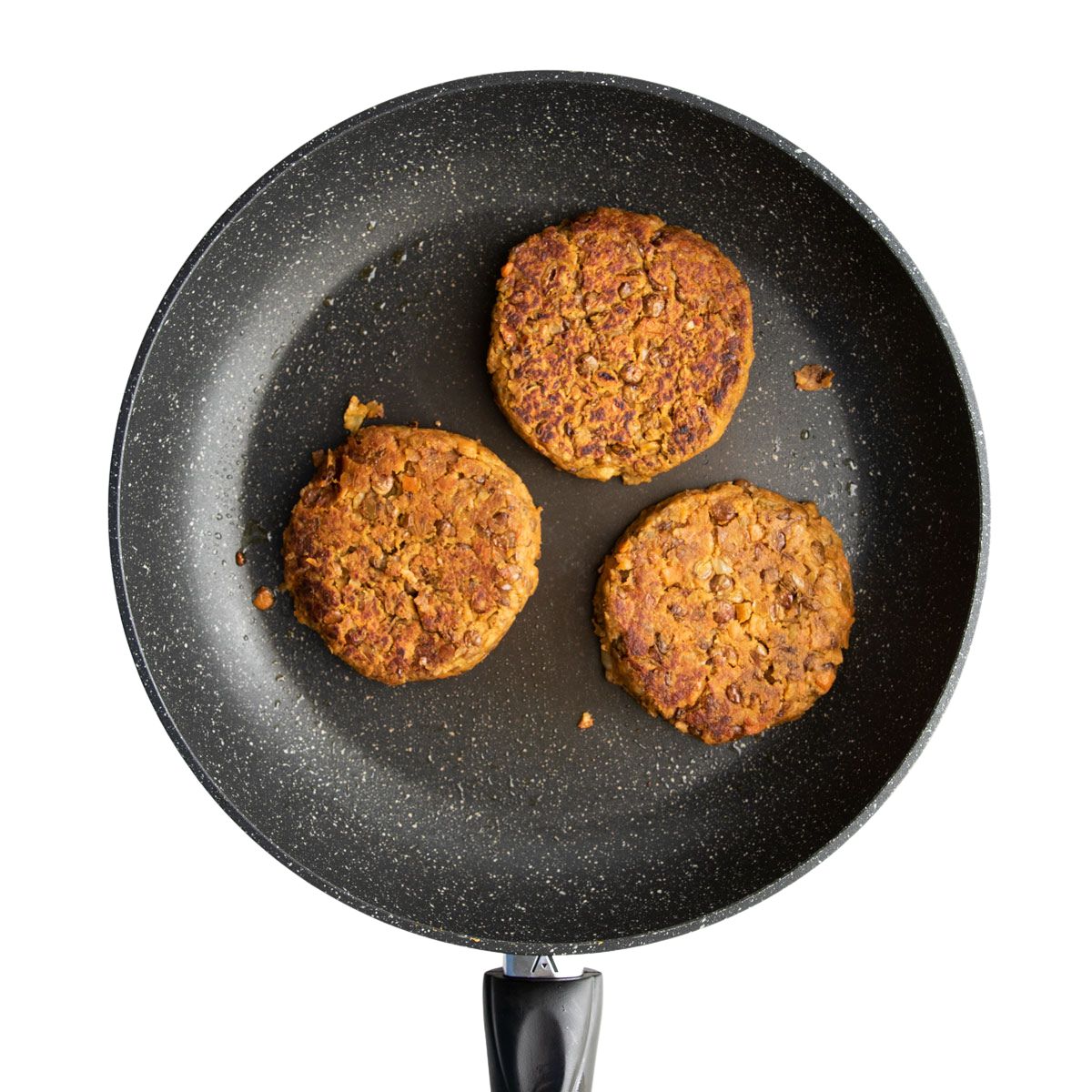 Three Lentil Burgers in Frying Pan.