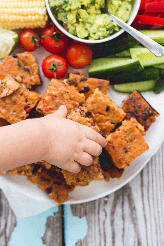 Chid's hand grabbing a piece of veggie lentil slice form a plate. 