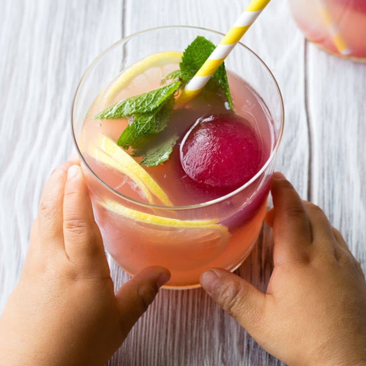 Child's Hands Holding Glass of Mocktail with Large Frozen Blueberry Icecube in It.