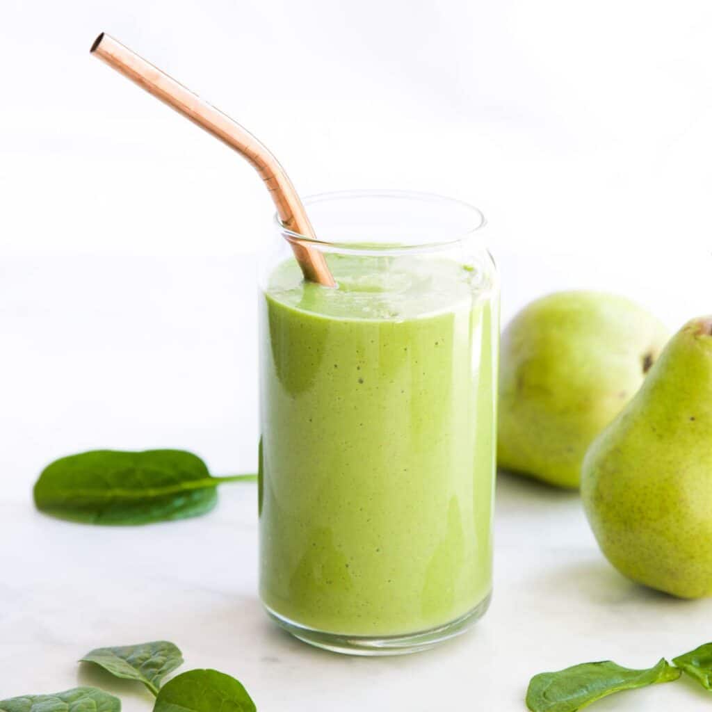 Side Shot of Pear Smoothie in Glass with Pear and Spinach Leaves Scattered in Background