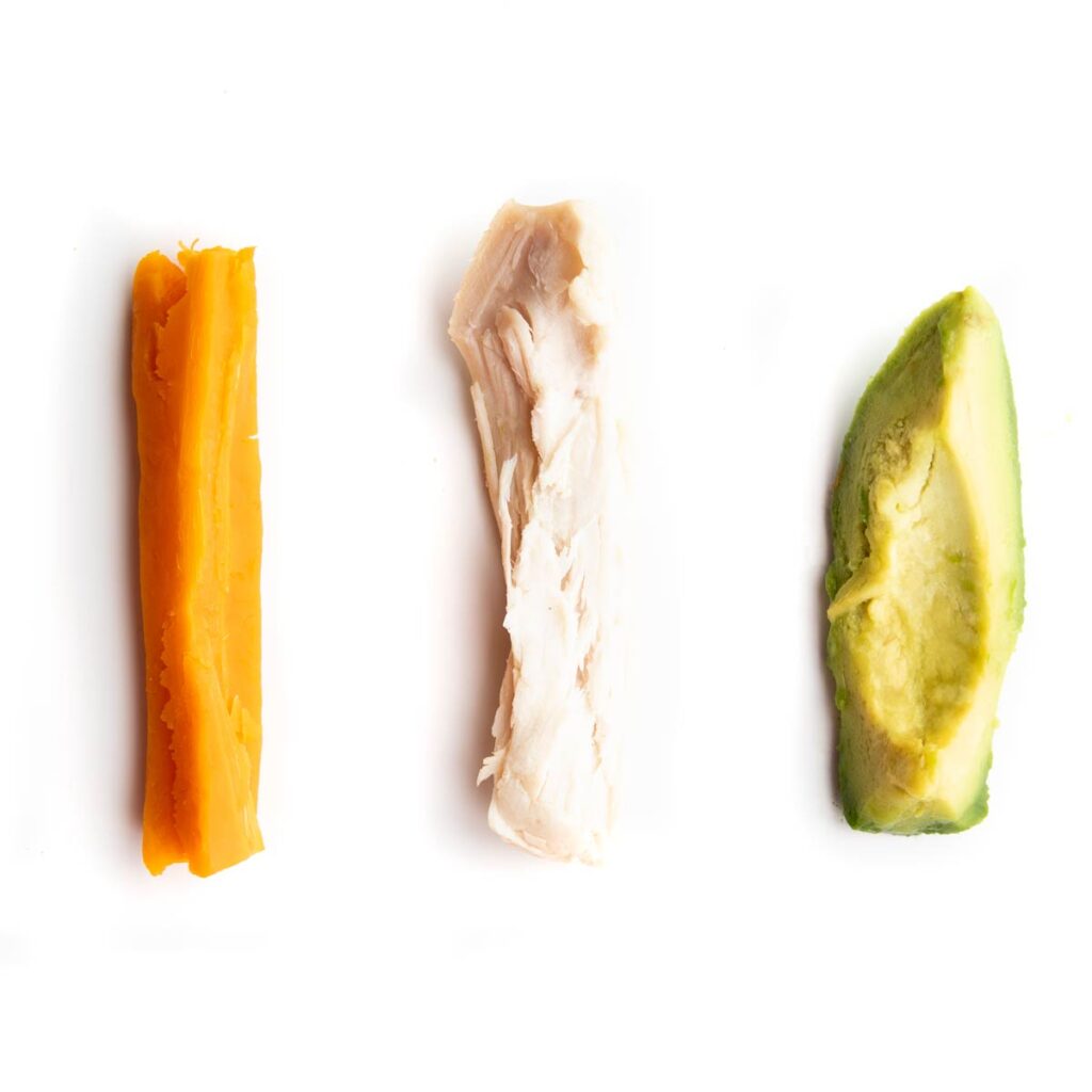 Cooked Carrot Stick, Cooked Chicken Thigh Shredded into Strip and Avocado Wedge on White Background