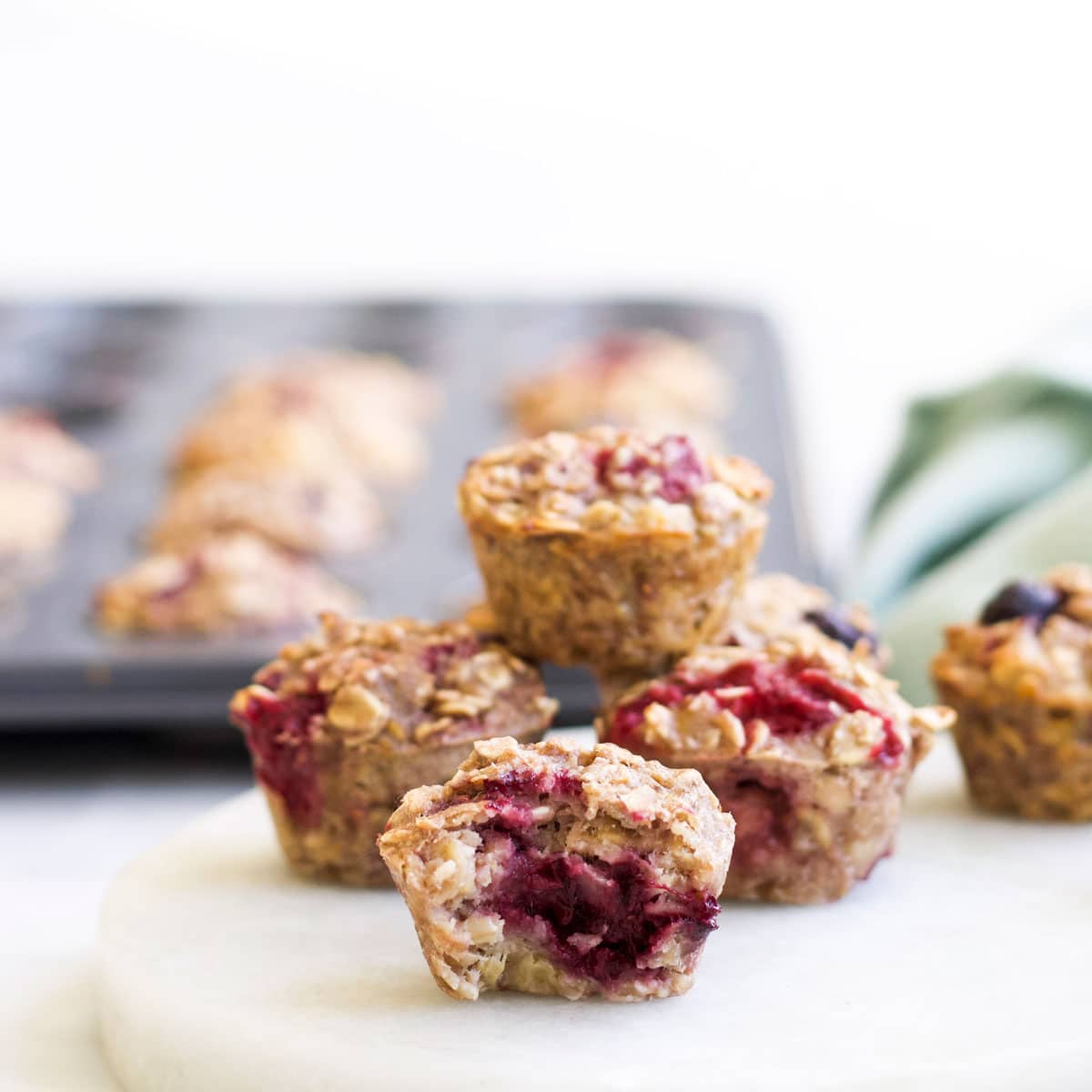 Stack of Baked Oatmeal Muffins on Marble Tray One with Bite Taken Out.  Muffin Tray in the Background. 