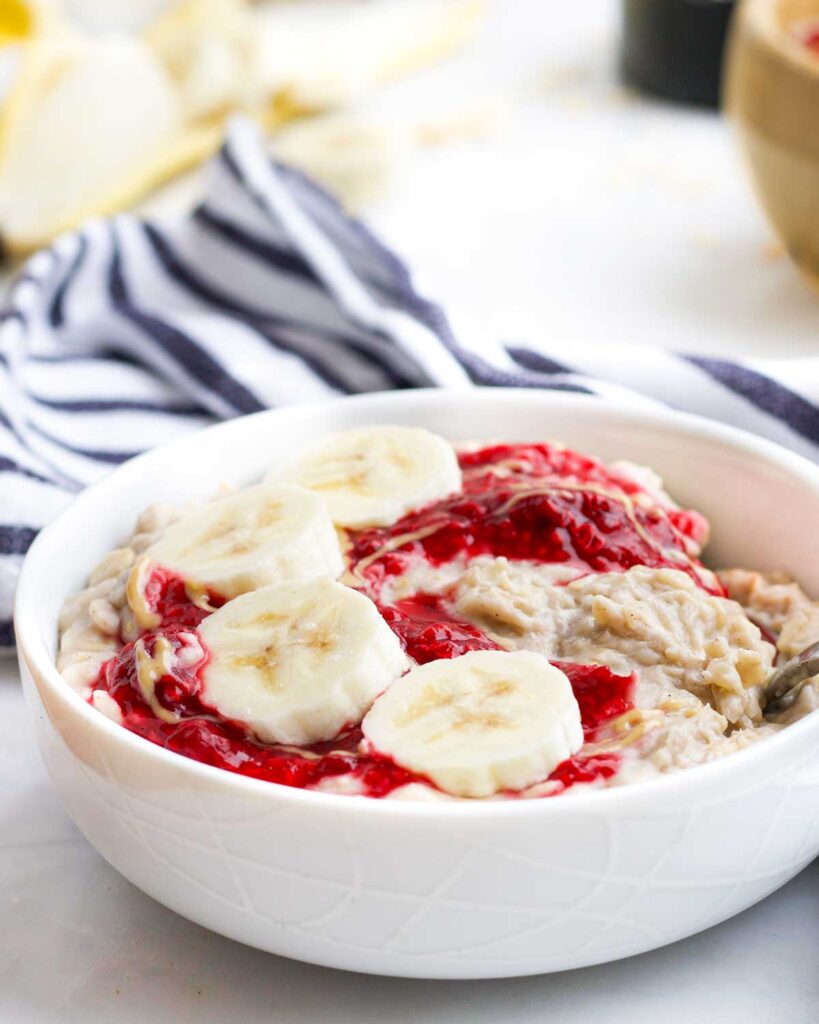 Side on Shot of Banana Porridge in Bowl Topped with Crushed Raspberries and Banana Slices