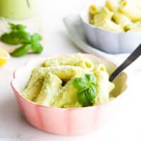 Bowl of Cooked Pasta Covered in a Creamy Basil Pesto Sauce and Garnished With Fresh Basil and Parmesan Cheese.