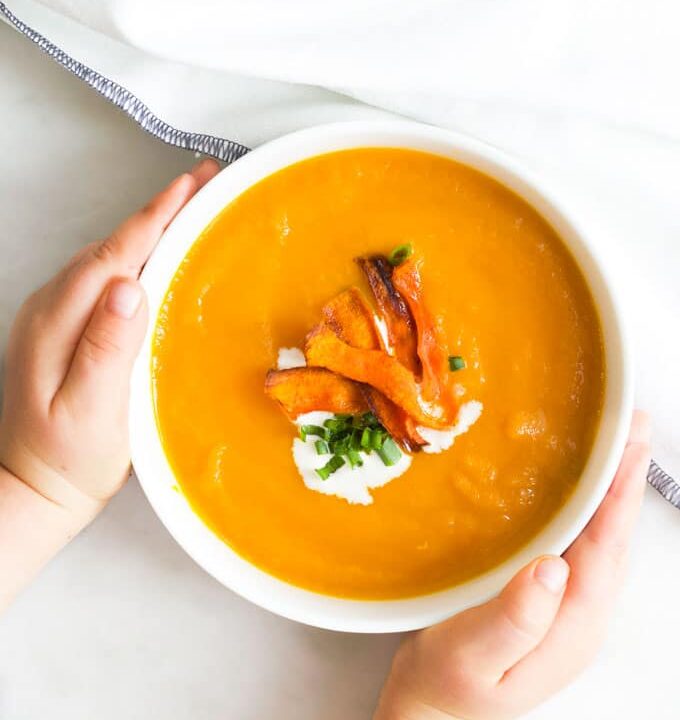 Child Grabbing Bowl of Carrot and Orange Soup