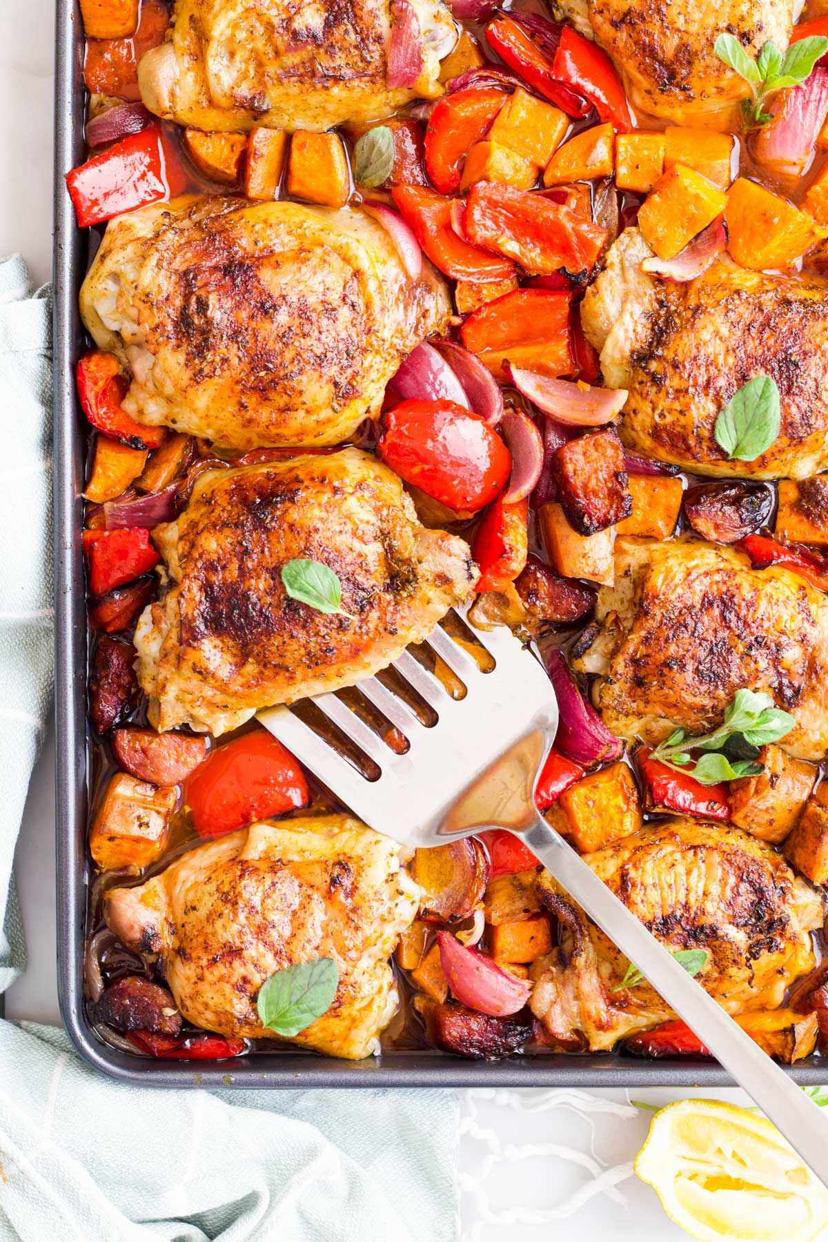 Chicken and Chorizo Tray Bake Cooked in Tray with Fish Slice About to Remove on Chicken Thigh from Tray.