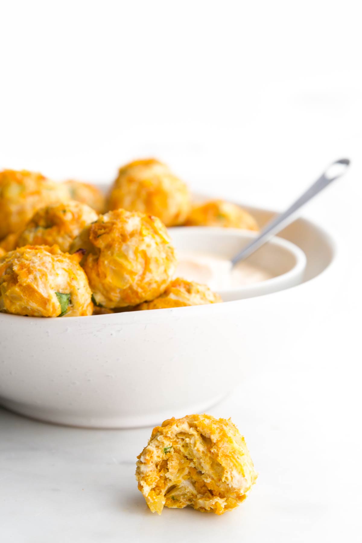 Chicken Meatballs in White Bowl Served with Dip and One Ball in Forefront with Bite Removed.