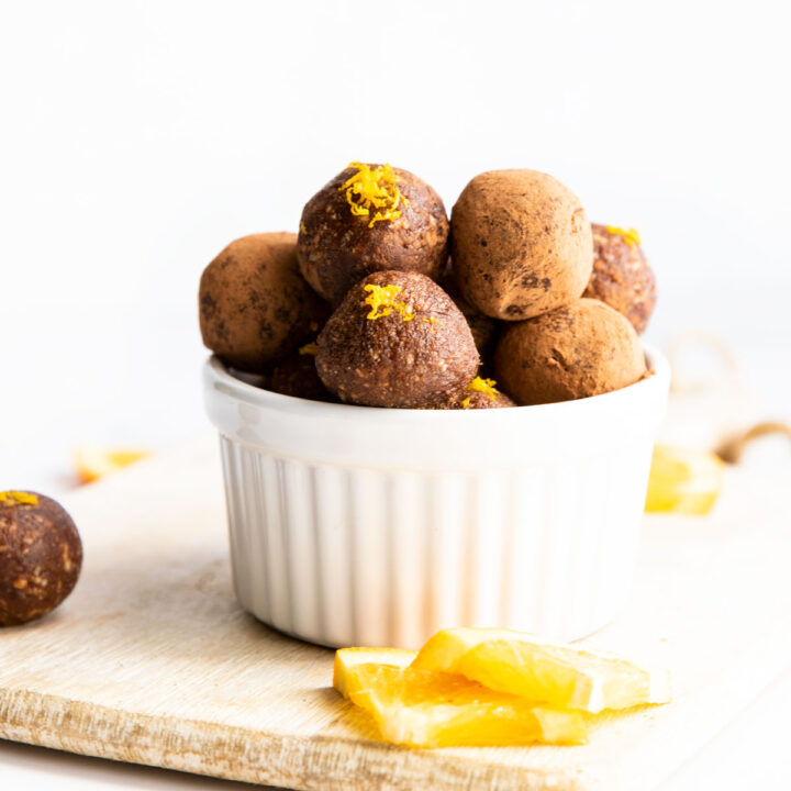 Chocolate Orange Bliss Balls in Small Bowl With Slices of Orange in the Foreground.