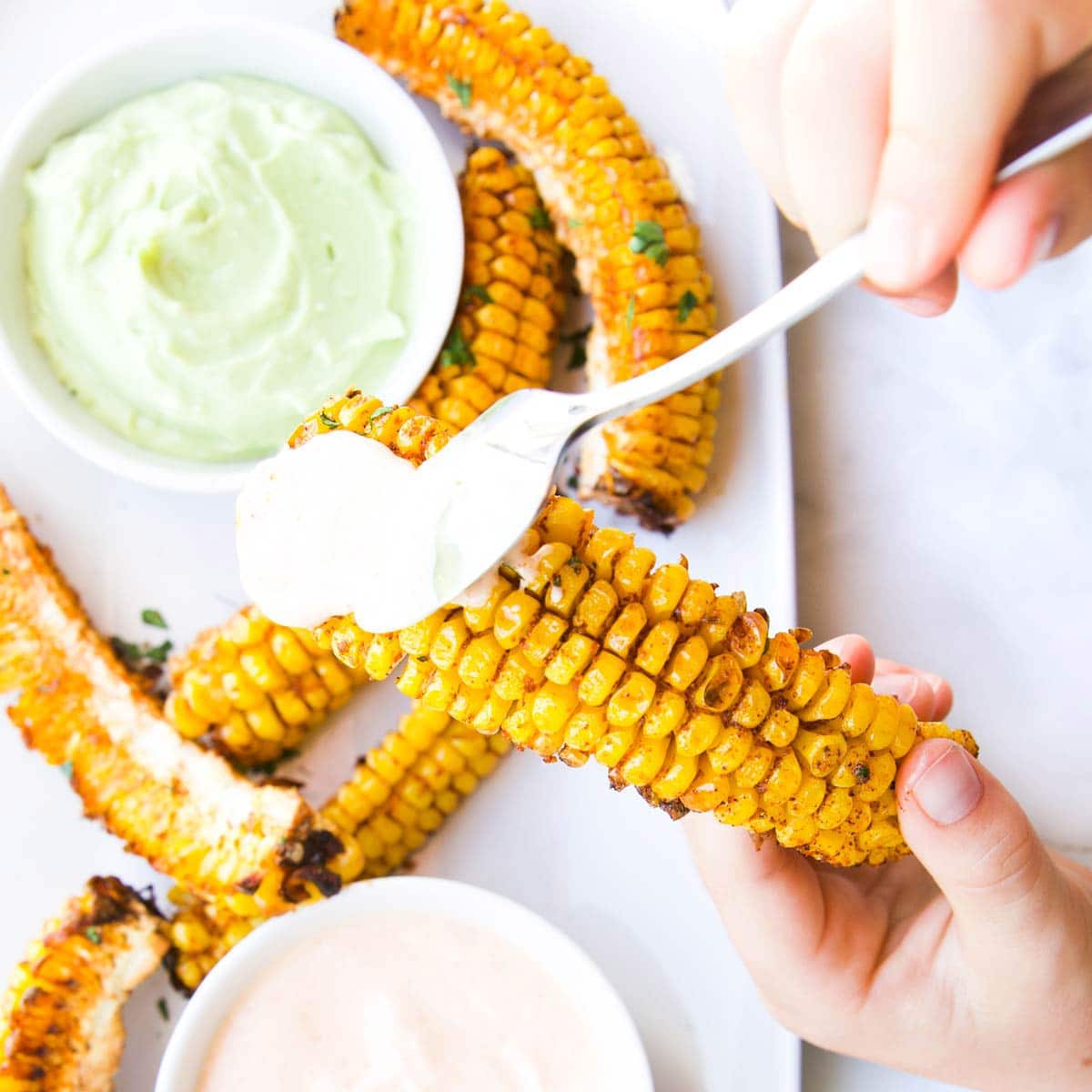 Child Picking Up a Corn Rib from Plate and Spooning Dip on Top.