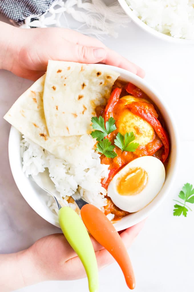 Child Holding Bowl of Egg Curry with Rice and Roti Bread