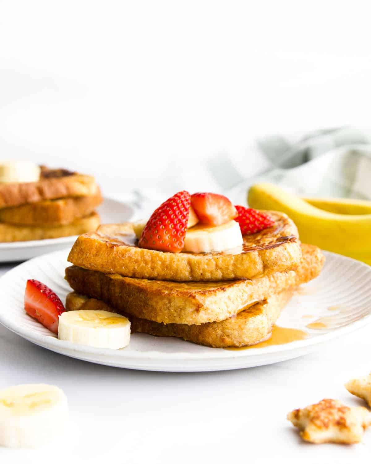 3 Slices of Banana French Toast Stacked on Plate Topped with Banana and Strawberry.