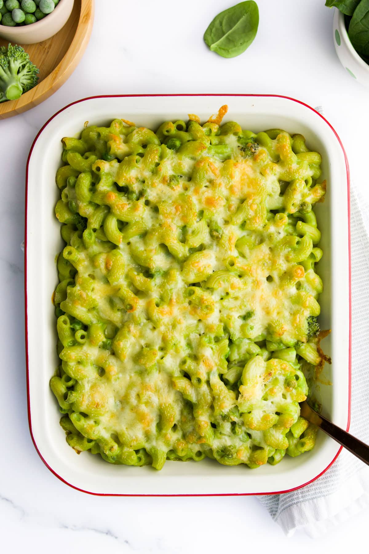 Baked Green Mac and Cheese in Baking Dish with Spinach, Peas and Broccoli in Background.