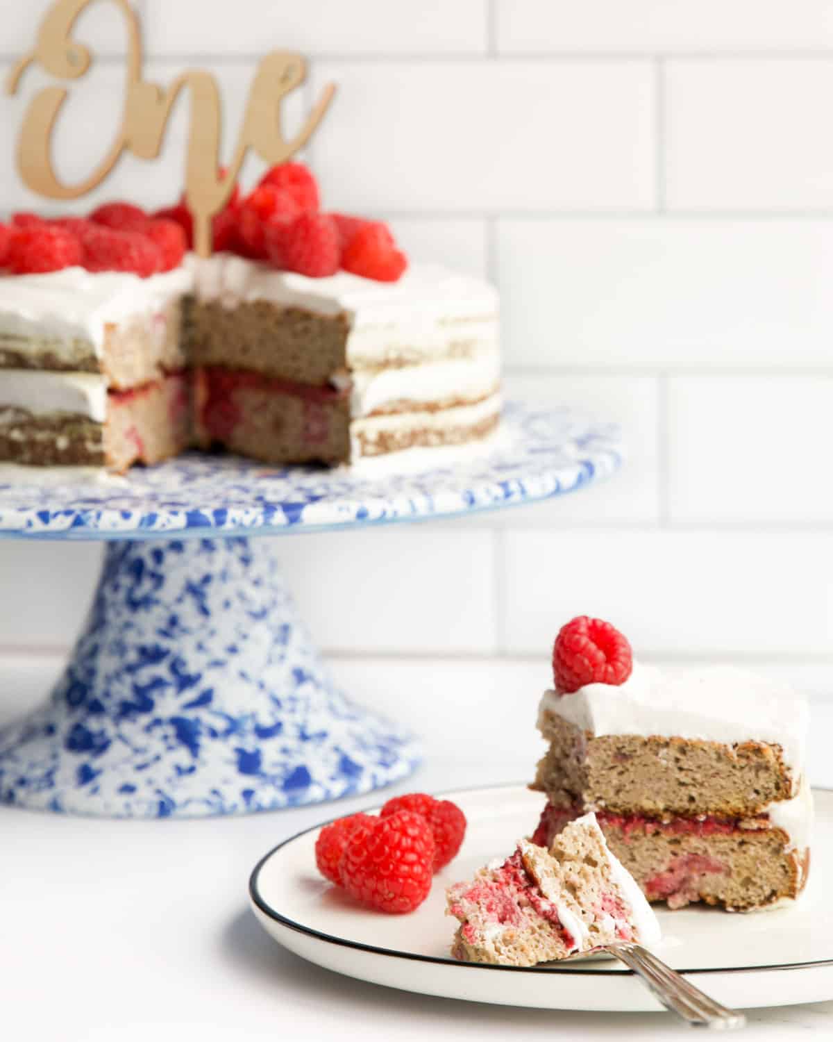 Slice of First Birthday Cake on Flat with Remaining Cake on Cake Stand in the Background.