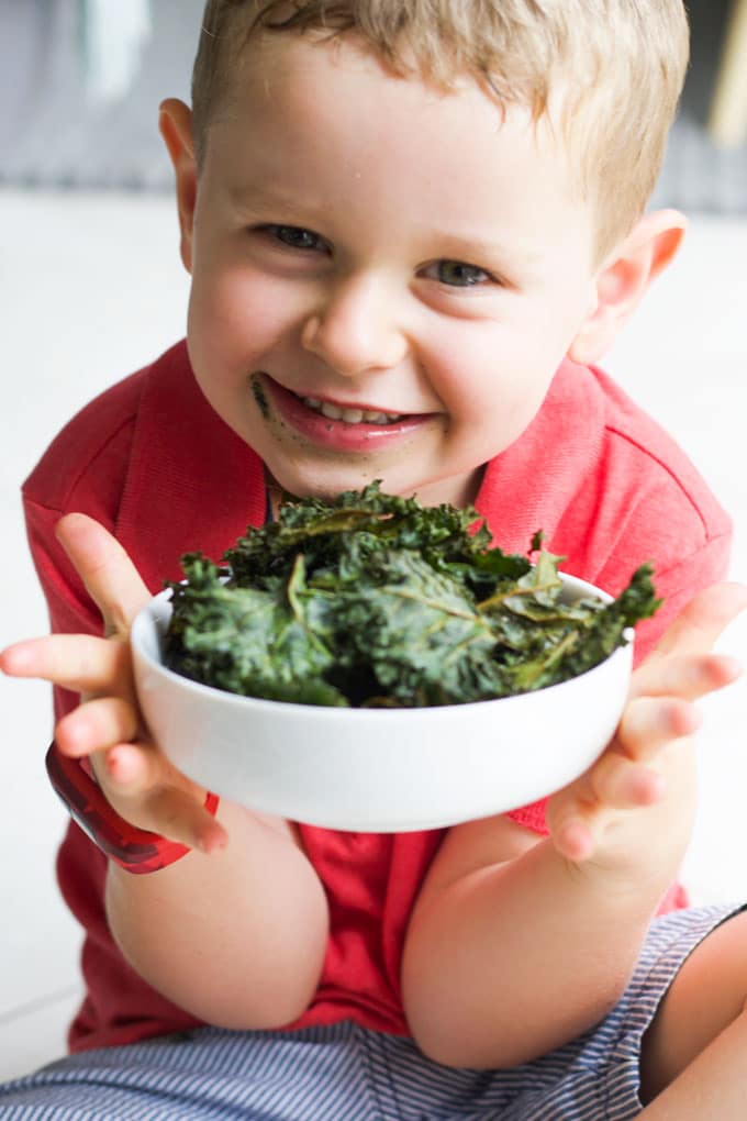 Child Smiling Holding a Bowl of Baked Kale Chips