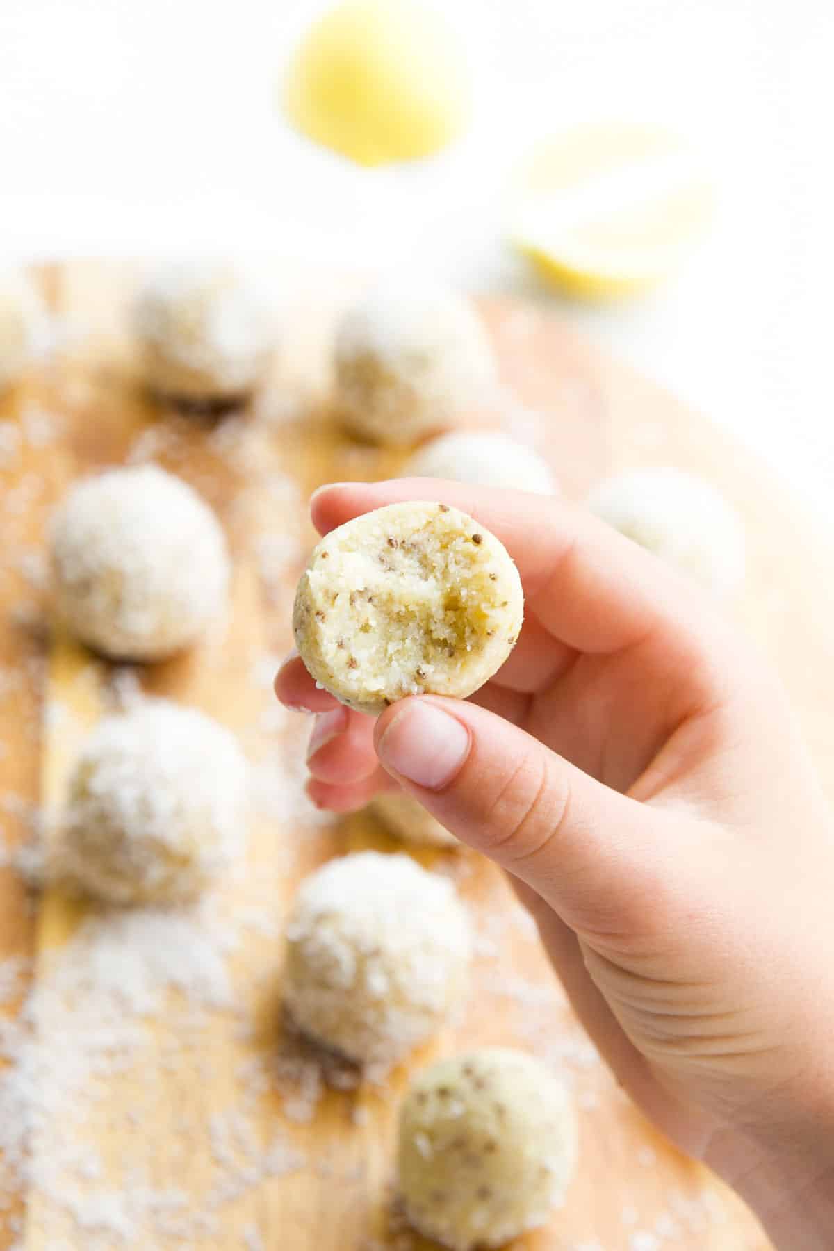 Hand Holding a Lemon Energy Ball with Bite Removed and Balls in the Background.