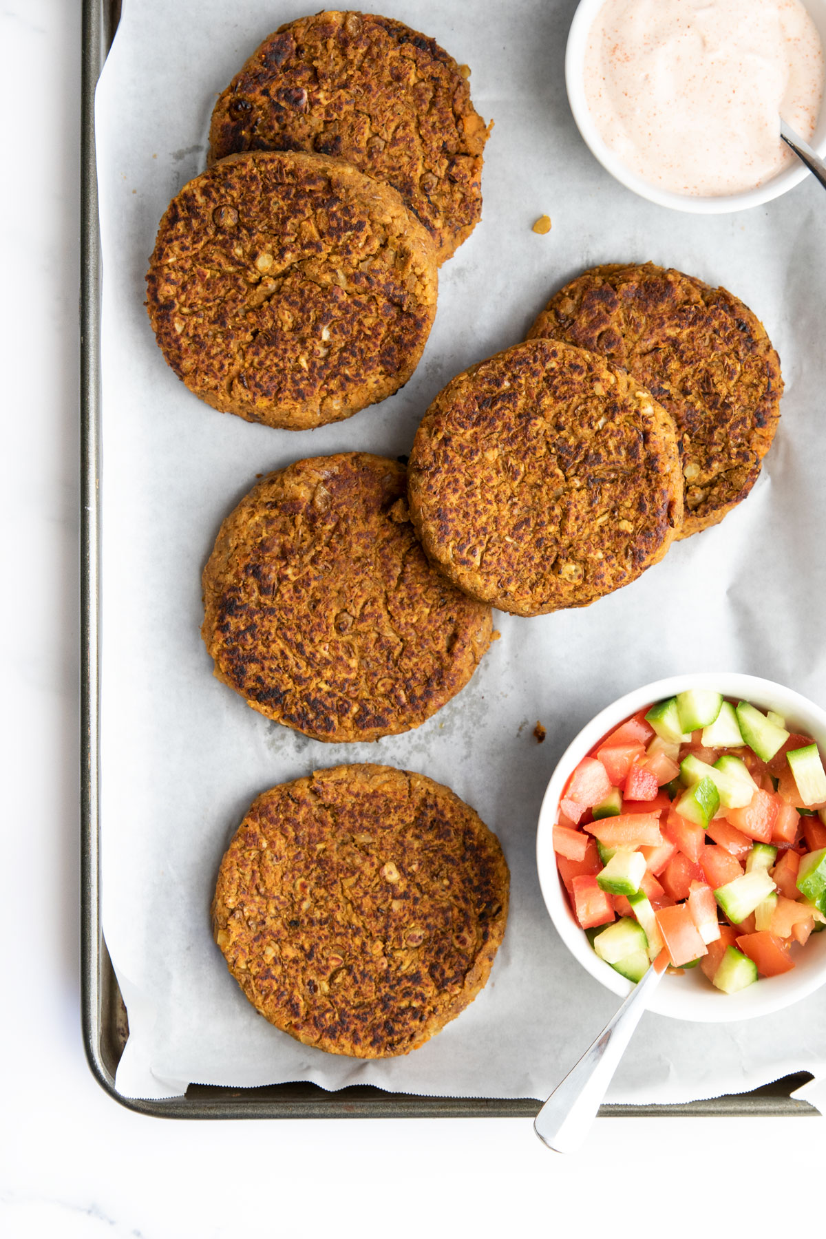 Lentil Burgers on TrayWith Sauce and a Tomato Cucumber Salad.