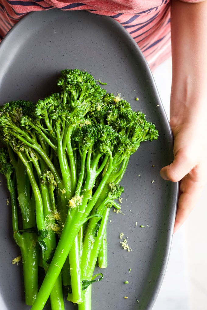 Child holding Plate of Sautéed Broccolini topped with Lemon Zest