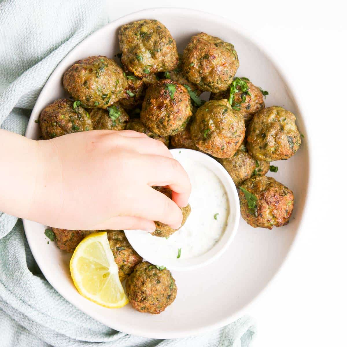 Child Dipping Spiced Meatball in Mint Yogurt Sauce.