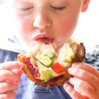 Child Eating A Sweet Potato Pizza Crust Topped with Tomato Sauce, Cheese and Avocado.