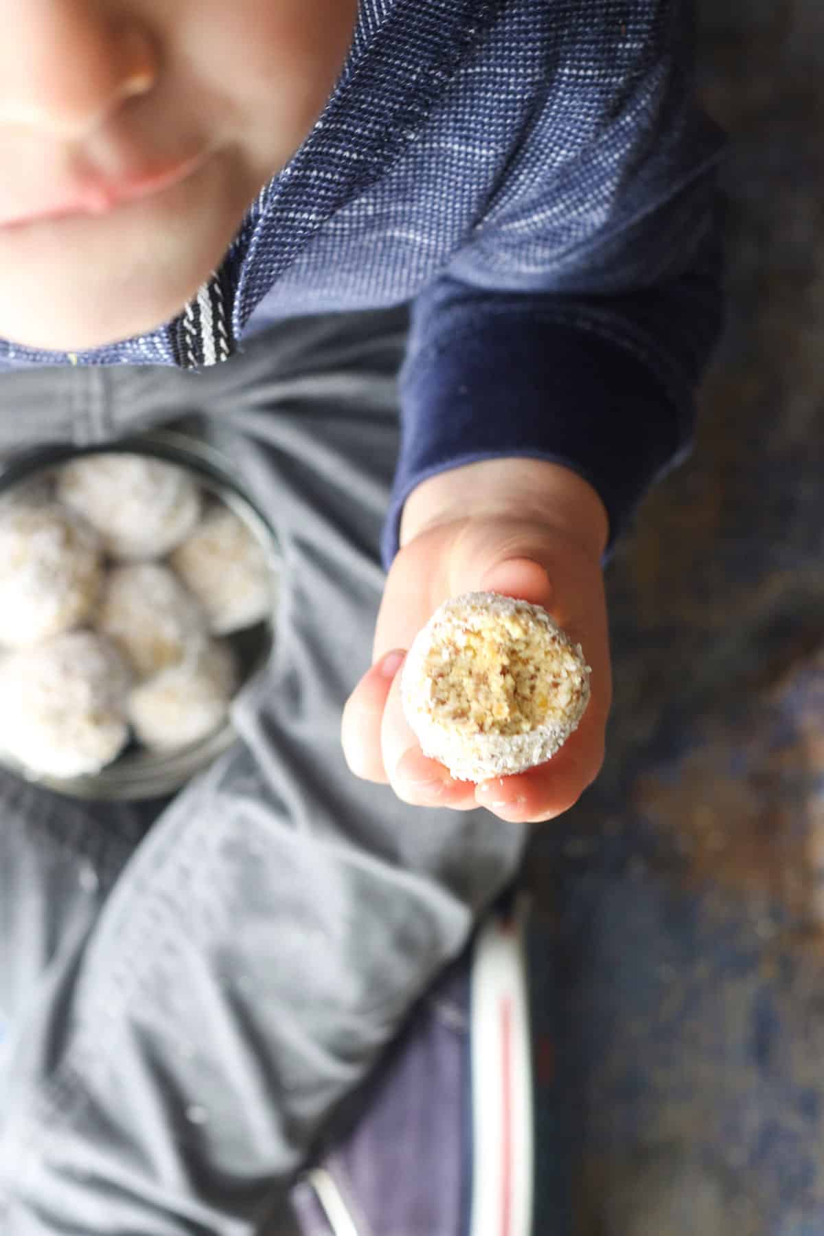 Child Holding Tropical Energy Ball with Bite Removed. 