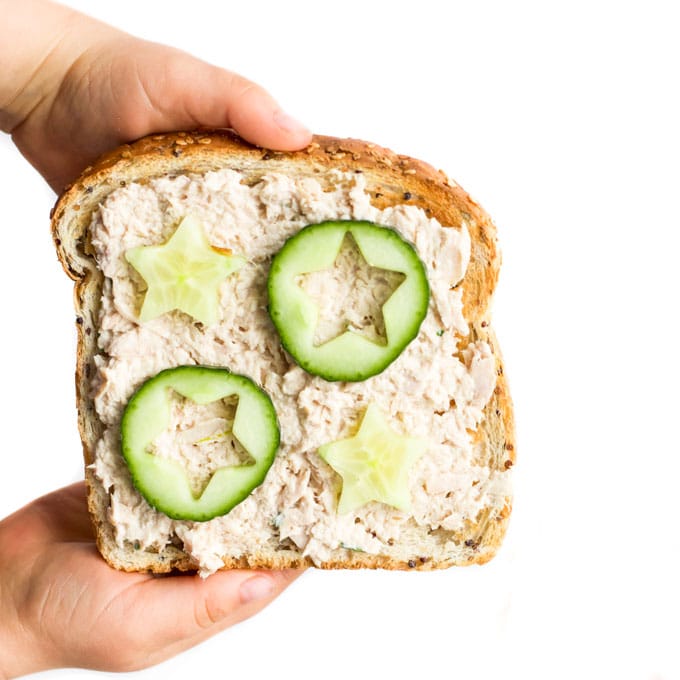 Child Holding Slice of Toast with a Toast Topping of Tuna and Cucumber