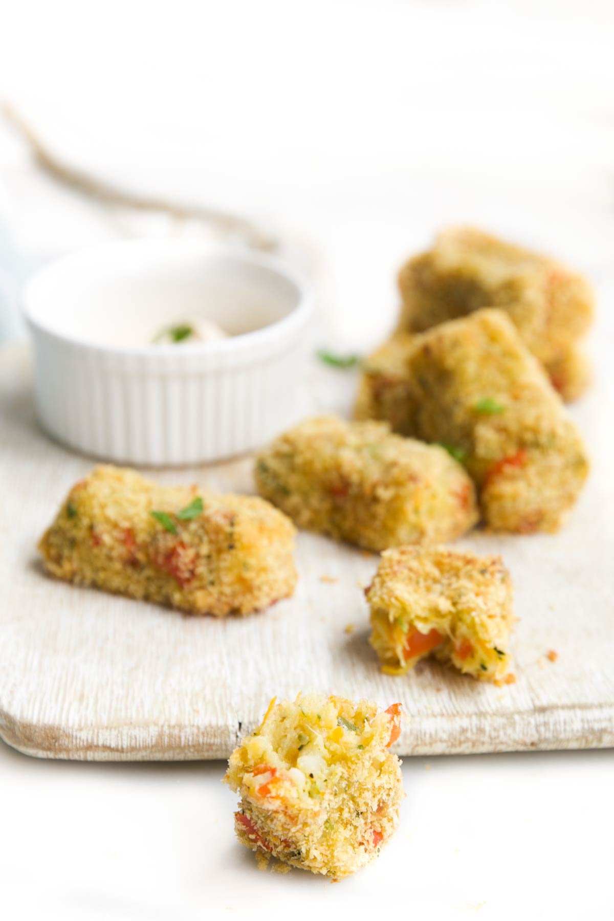 Side Shot of Vegetable Croquettes on Small Wooden Board with Dip. One Croquette at Forefront with Bite Removed