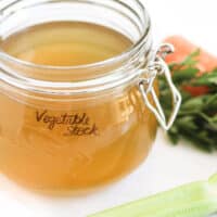 Vegetable Stock in Glass Jar with Vegetables Scattered in Background.