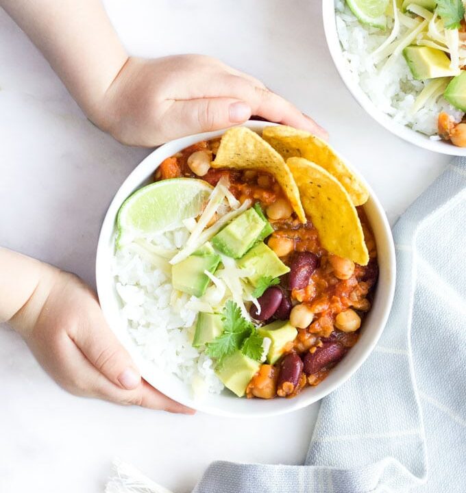 Child Grabbing Bowl of Vegetarian Chilli Topped with Cheese , Avocado and Corn Chips