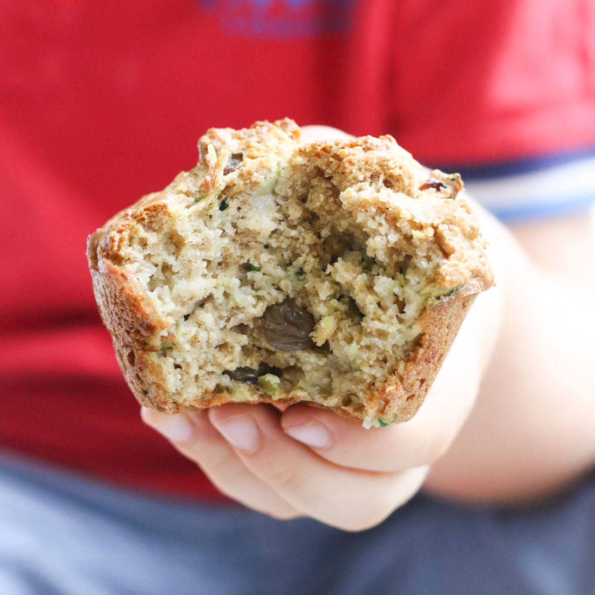 Child Holding a Zucchini Muffin with Bite Out.