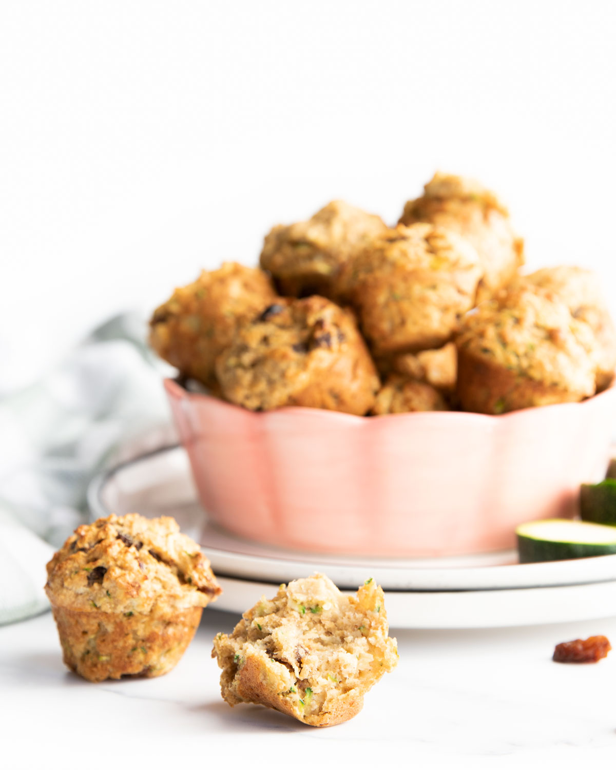 Zucchini Muffins in Bowl with Muffin with Bite Removed at Front.